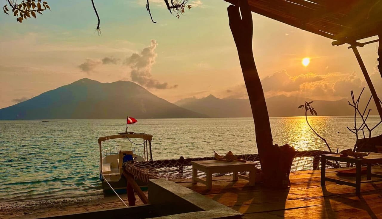 Sunset over the Pantar Strait from the resort beach deck, dive boat moored at the jetty